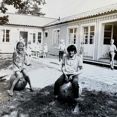 Flicka och pojke studsar på leksaker på kollo. Andra barn i bakgrunden.