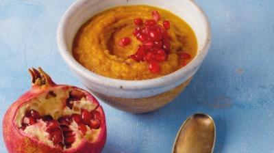 Skål med pumpagröt i och granatäppelkärnor på toppen. Ett granatäpple och sked bredvid.