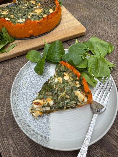 En bit sötpotatispaj med fetaost och spenat på en tallrik med färsk spenat på sidan om