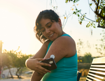 Kvinna läser av sin cgm-mätare på armen med mobilen