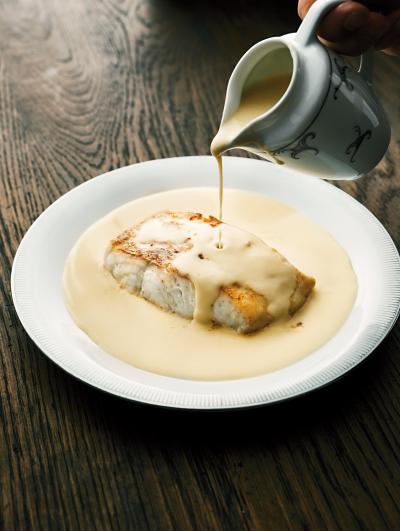 Panerad fisk på en tallrik och Senapssås runt och som hälls på ur en liten såskanna